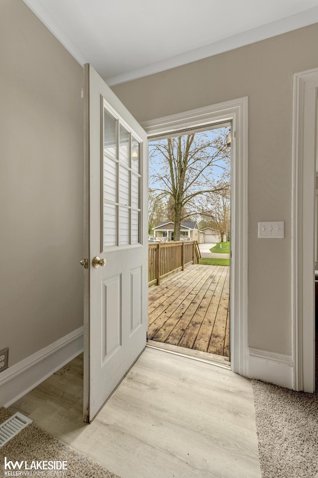 doorway to outside featuring baseboards, crown molding, visible vents, and wood finished floors