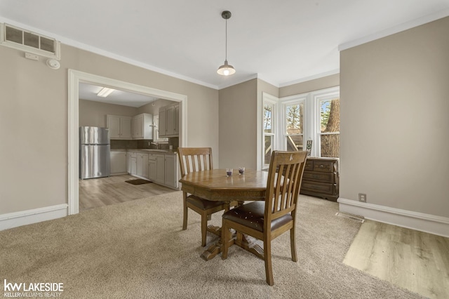 dining room featuring baseboards, crown molding, light wood finished floors, and visible vents
