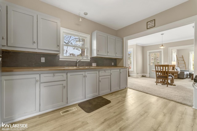 kitchen featuring a sink, pendant lighting, light wood-type flooring, visible vents, and backsplash