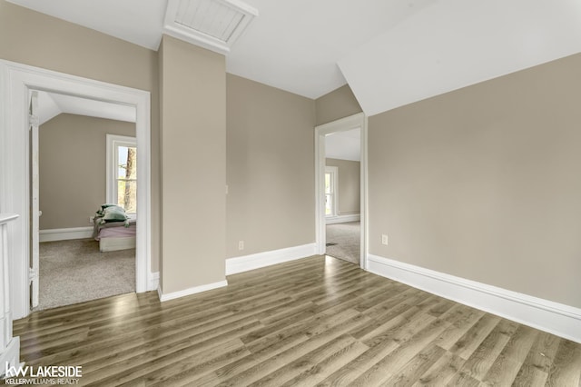 spare room with vaulted ceiling, a wealth of natural light, baseboards, and wood finished floors