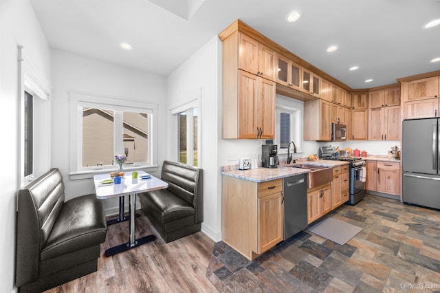 kitchen with a sink, stainless steel appliances, light stone counters, recessed lighting, and glass insert cabinets