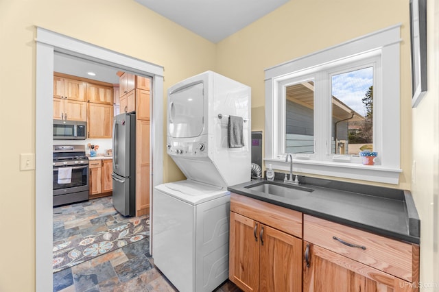 washroom with stone finish floor, stacked washer and clothes dryer, and a sink