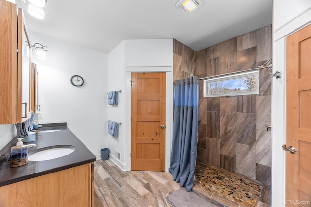 bathroom with double vanity, wood finished floors, a tile shower, a sink, and visible vents