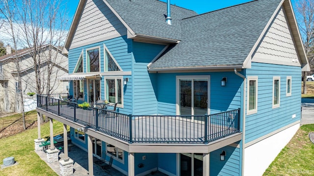 rear view of house with roof with shingles, a deck, a patio, and a lawn