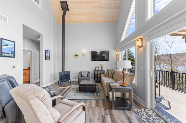 living area featuring baseboards, a wood stove, high vaulted ceiling, and wood finished floors