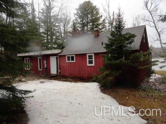 rear view of house featuring board and batten siding, roof with shingles, and a chimney