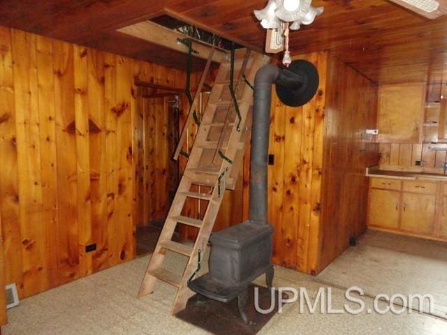 interior space with wooden ceiling, a wood stove, wood walls, and light colored carpet
