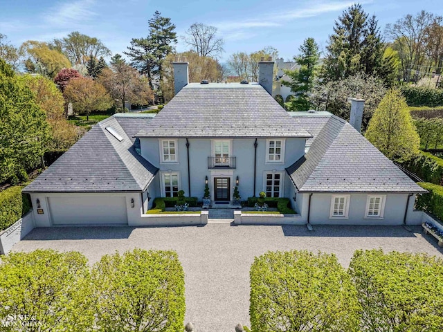 view of front of home with a chimney, a balcony, a garage, a high end roof, and stucco siding