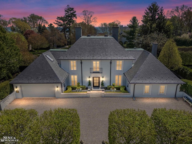 view of front facade featuring stucco siding, a high end roof, a chimney, and a balcony