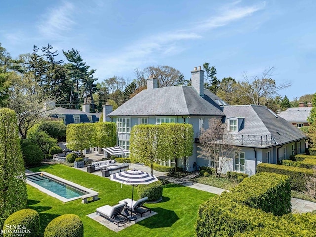 back of house featuring a high end roof, a patio, a chimney, and a lawn
