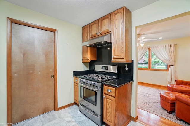 kitchen featuring a ceiling fan, dark countertops, gas range, baseboards, and under cabinet range hood