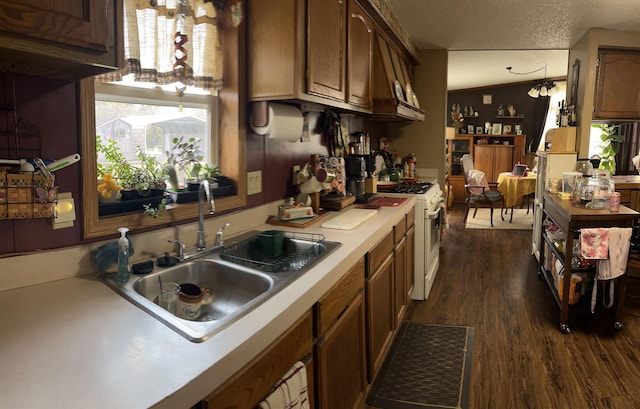 kitchen with a sink, a textured ceiling, white gas range, light countertops, and dark wood-style floors