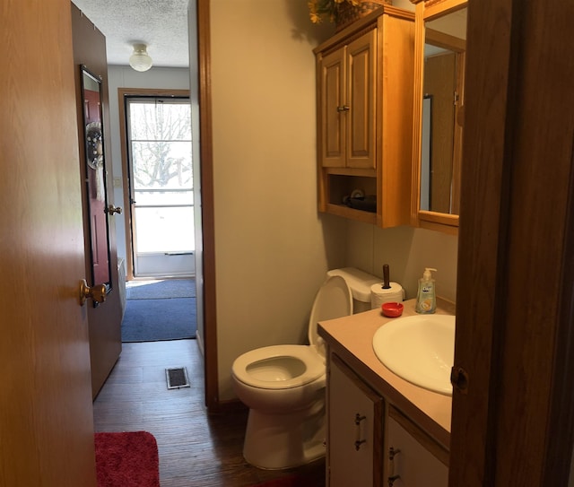 half bathroom with a textured ceiling, toilet, visible vents, vanity, and wood finished floors