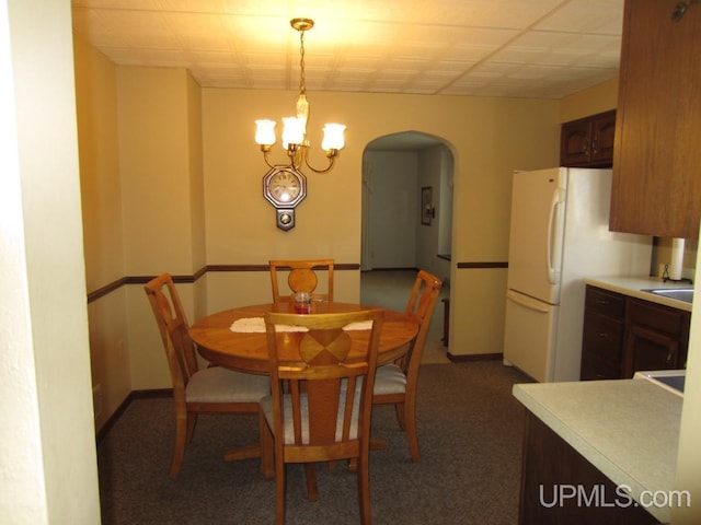 dining area featuring arched walkways, carpet flooring, an inviting chandelier, and baseboards