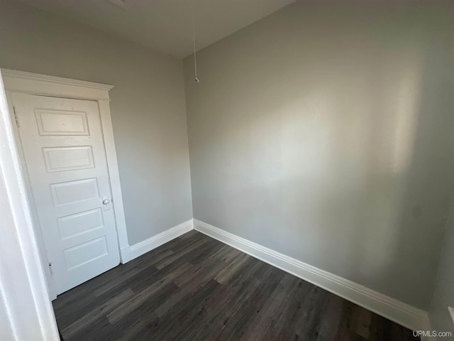 unfurnished room featuring attic access, dark wood-style flooring, and baseboards