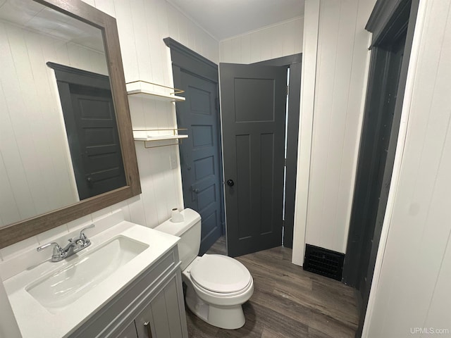 half bath featuring crown molding, toilet, wood finished floors, and vanity