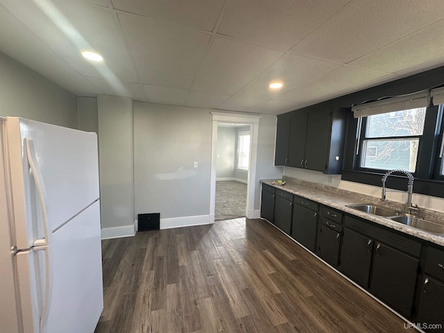 kitchen featuring freestanding refrigerator, dark cabinets, a sink, dark wood-type flooring, and light countertops