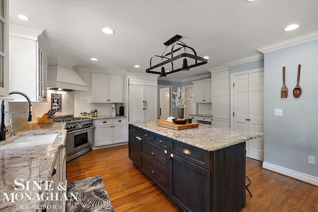 kitchen featuring stainless steel stove, a sink, custom exhaust hood, white cabinetry, and recessed lighting