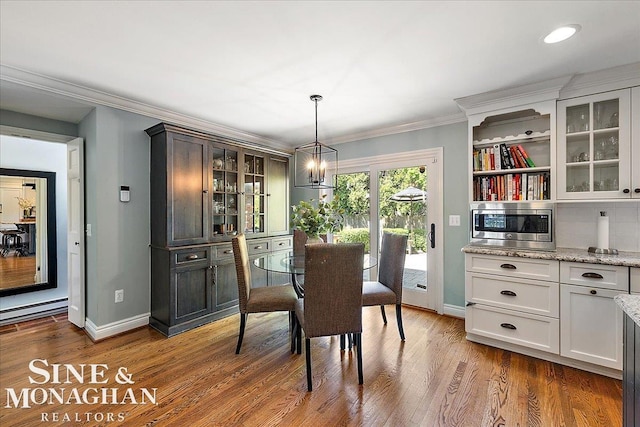 dining room featuring baseboards, ornamental molding, wood finished floors, a chandelier, and a baseboard heating unit
