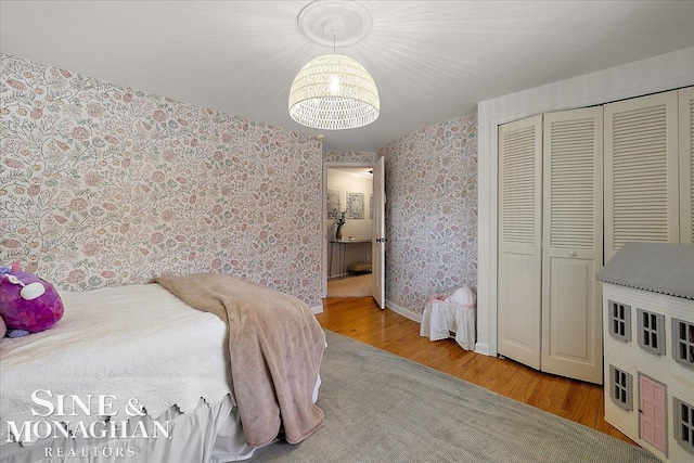 bedroom featuring wallpapered walls, wood finished floors, a chandelier, a closet, and baseboards