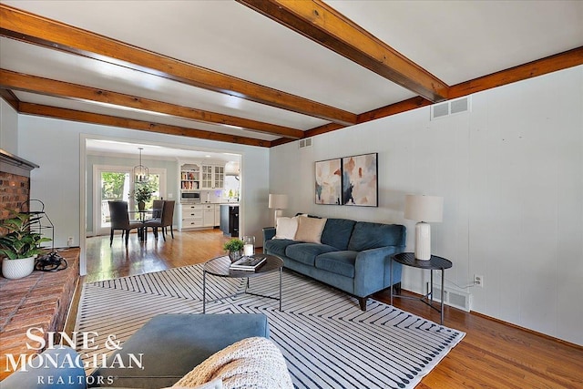 living room featuring wood finished floors, beamed ceiling, and a chandelier