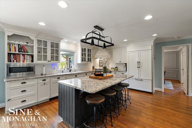 kitchen with built in appliances, ornamental molding, white cabinetry, a center island, and recessed lighting