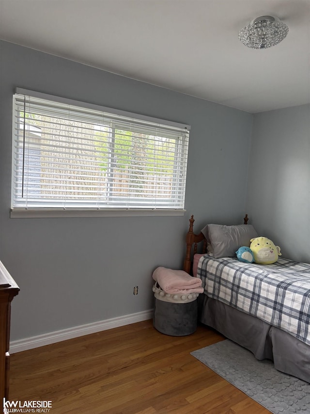 bedroom with multiple windows, wood finished floors, and baseboards