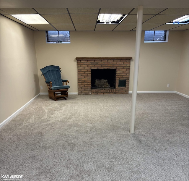 finished basement featuring carpet flooring, a paneled ceiling, baseboards, and a brick fireplace