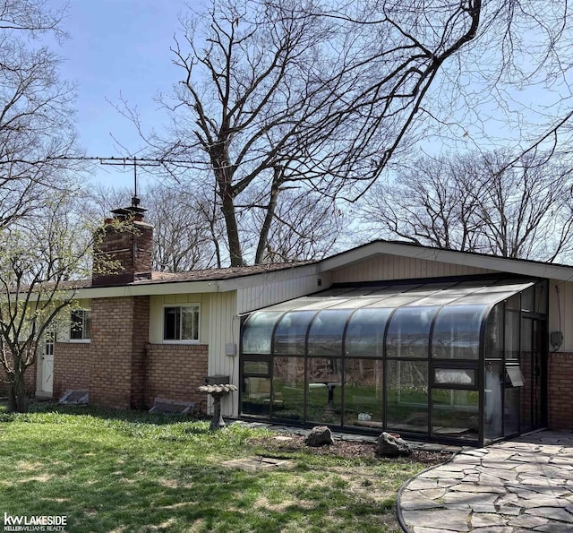 view of side of property with a sunroom, brick siding, a chimney, and a lawn