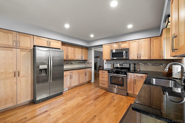 kitchen featuring stainless steel appliances, a sink, light wood-style flooring, light brown cabinets, and tasteful backsplash