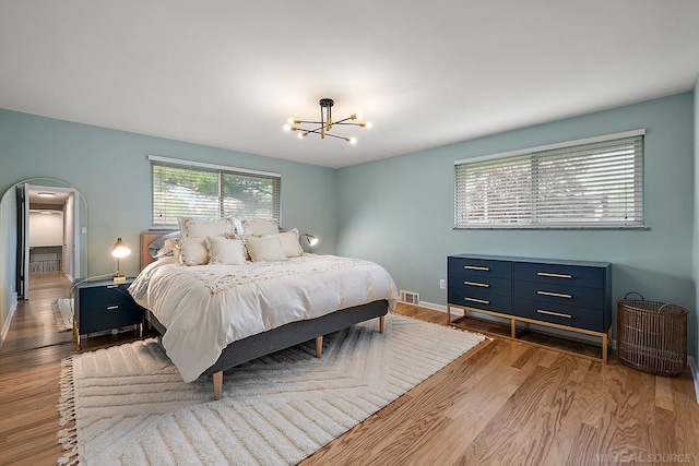 bedroom featuring wood finished floors, arched walkways, a chandelier, and baseboards