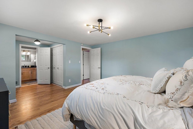 bedroom featuring wood finished floors, a chandelier, baseboards, a closet, and ensuite bathroom
