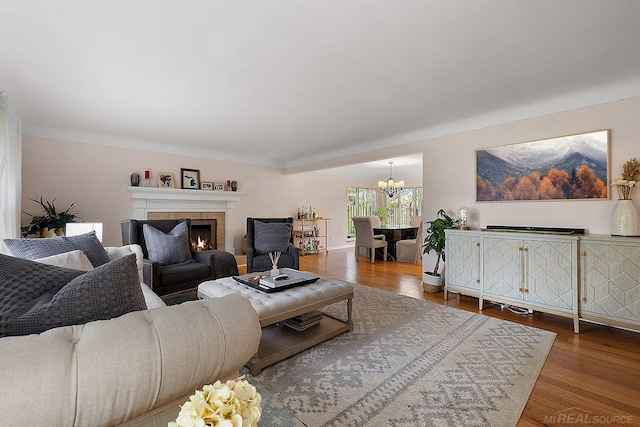 living room featuring a chandelier, wood finished floors, and a warm lit fireplace