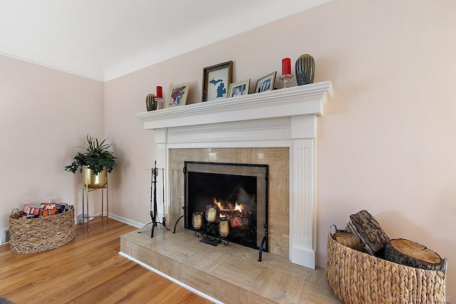 detailed view of a fireplace, wood finished floors, and baseboards
