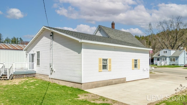 view of side of property with a chimney, a yard, a wooden deck, roof with shingles, and a patio area