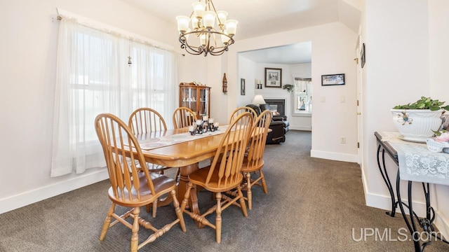 dining room with a chandelier, dark carpet, baseboards, and a glass covered fireplace