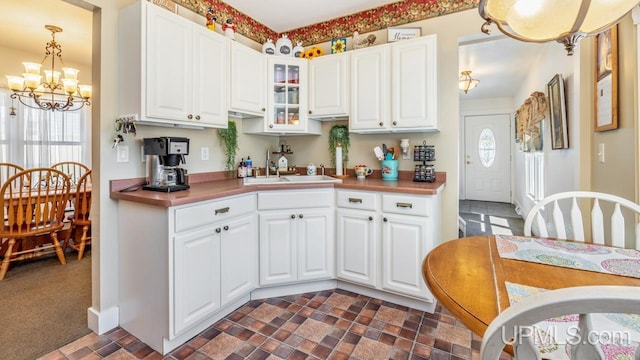 kitchen featuring a chandelier, a sink, glass insert cabinets, and white cabinets