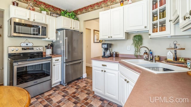 kitchen featuring appliances with stainless steel finishes, a sink, white cabinets, light countertops, and glass insert cabinets