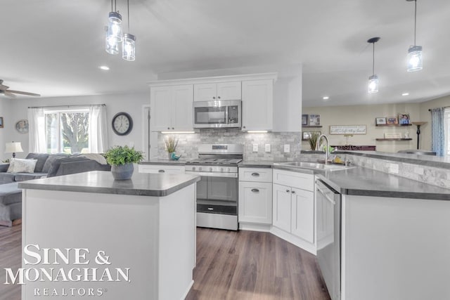 kitchen featuring stainless steel appliances, a sink, open floor plan, dark wood-type flooring, and a peninsula