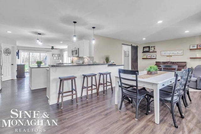 dining area with a barn door, dark wood-style floors, recessed lighting, a ceiling fan, and baseboards
