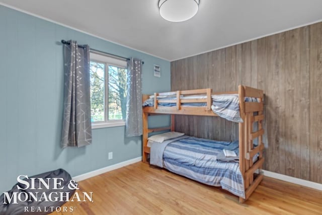 bedroom with wood finished floors, baseboards, and wood walls
