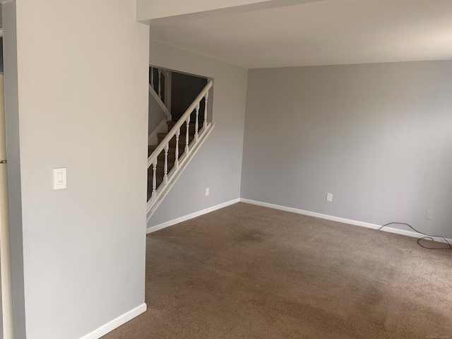 empty room featuring dark carpet, baseboards, and stairway