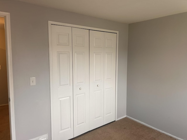 unfurnished bedroom with dark colored carpet, a closet, and baseboards