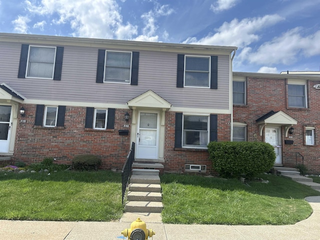townhome / multi-family property featuring entry steps, a front lawn, and brick siding