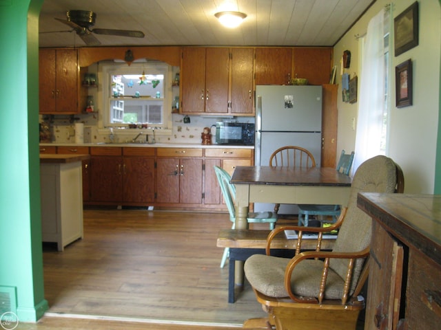 kitchen featuring brown cabinetry, black microwave, light wood-style flooring, freestanding refrigerator, and wooden ceiling