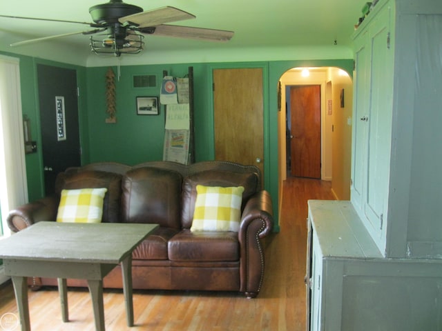 living area with arched walkways, light wood-style floors, and ceiling fan