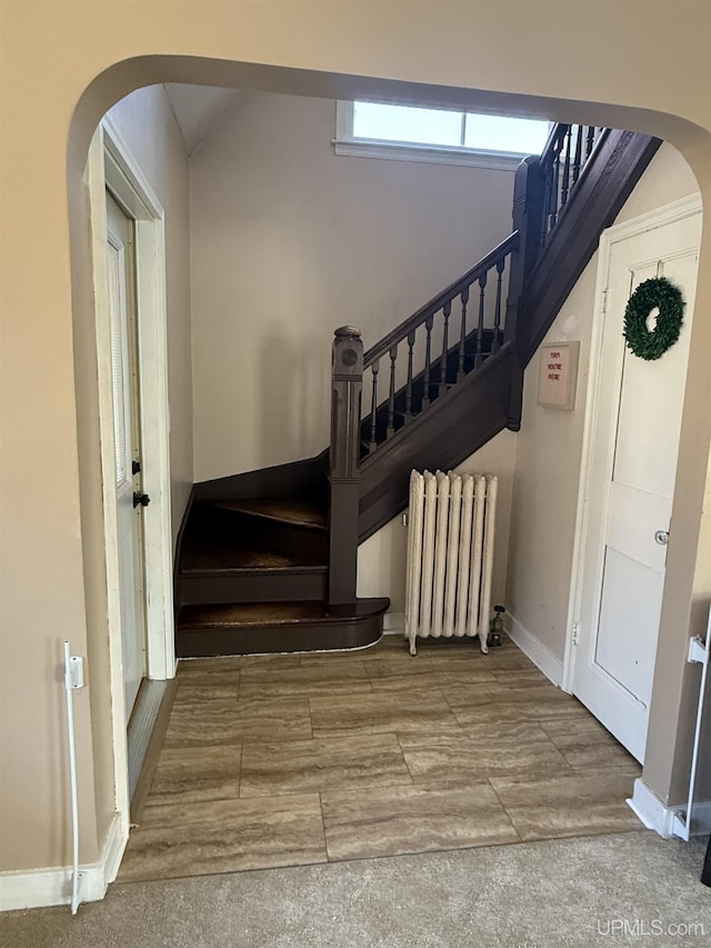 stairs featuring radiator heating unit, arched walkways, baseboards, and wood finished floors