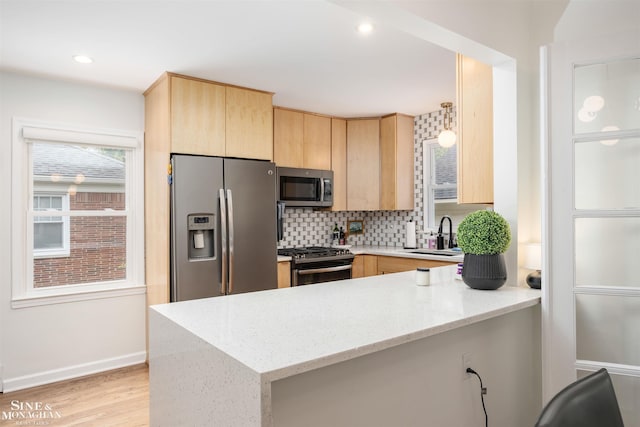 kitchen with stainless steel appliances, light brown cabinetry, a peninsula, tasteful backsplash, and light stone counters