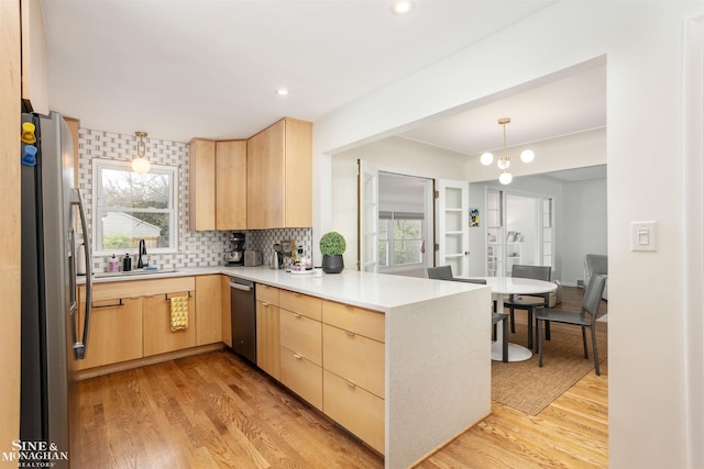 kitchen with stainless steel appliances, light brown cabinets, a peninsula, a sink, and light wood finished floors