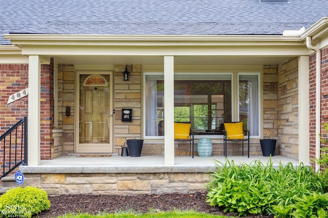 property entrance featuring covered porch, roof with shingles, brick siding, and stone siding